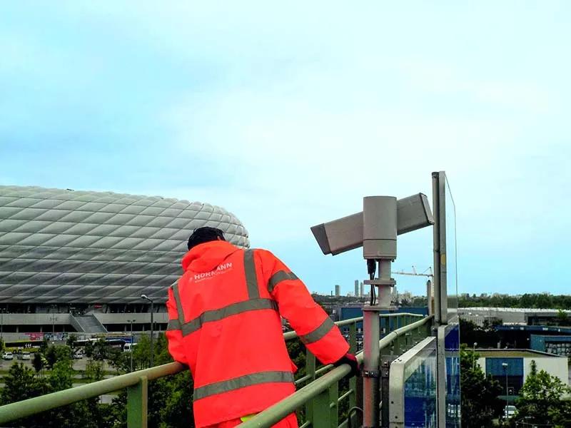 Mitarbeiter bei der Wartung einer Autobahnkamera, im Hintergrund die Allianz Arena